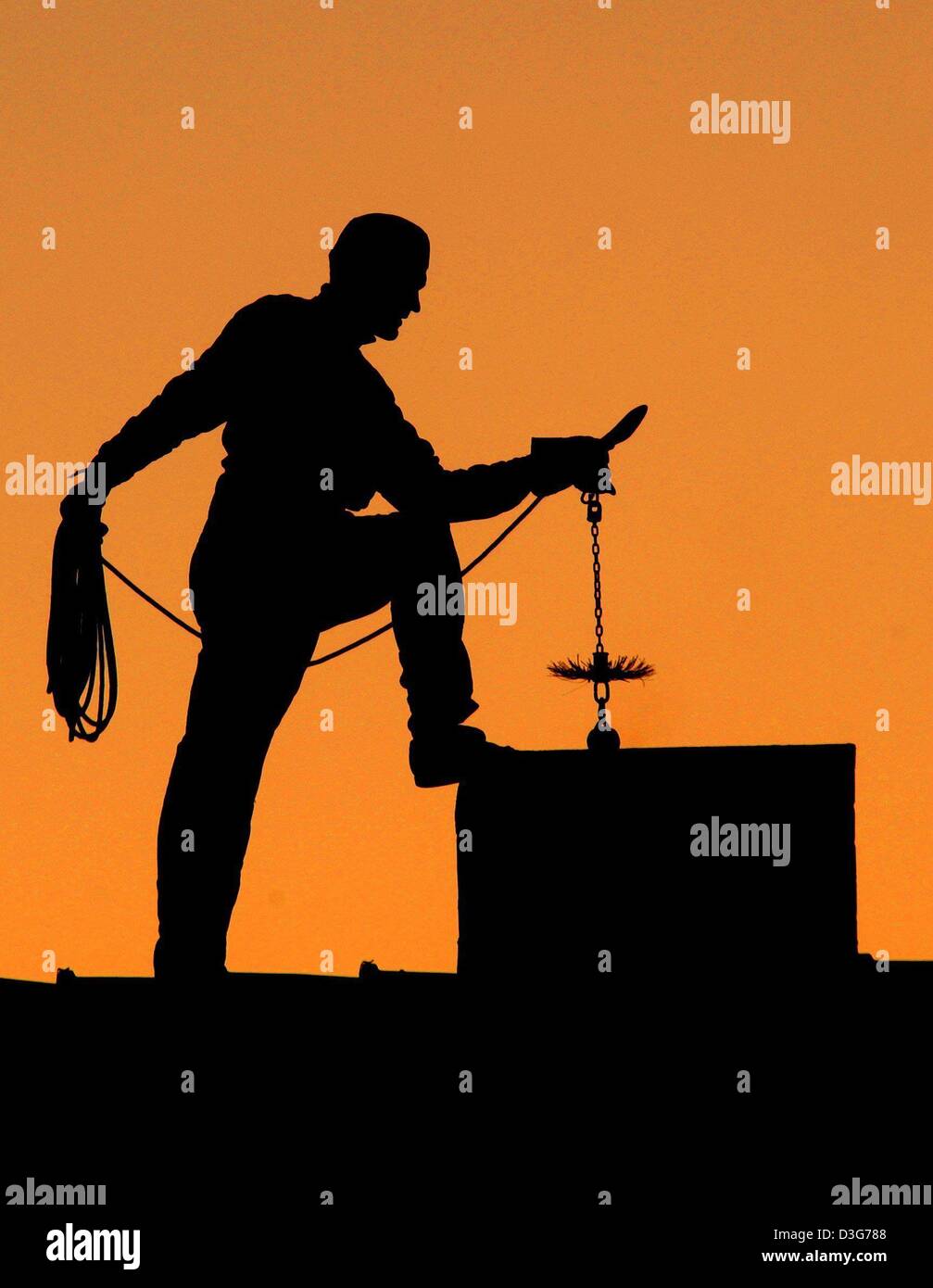 (dpa) - The silhouette of a chimney sweep is seen at work against the orange sky at dawn in Muellrose, Germany, 12 November 2003. At the beginning of winter the high season for chimney sweeps has started as they have to clear the chimneys of soot to attain ideal heating conditions for ovens. Stock Photo