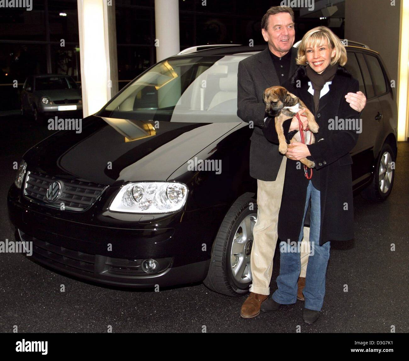 (dpa) - German chancellor Gerhard Schroeder and his wife Doris Schroeder-Koepf hold their terrier Holly in their arms and smile as they stand in front of their new VW Touran van at the delivery department of the VW assembly plant in Wolfsburg, Germany, 2 November 2003. Stock Photo