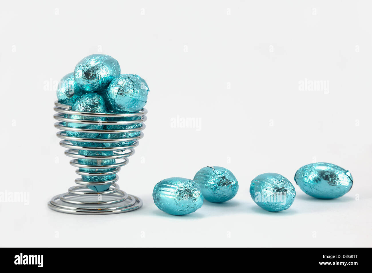 Bright blue small foil wrapped easter eggs in a wire eggcup. Stock Photo