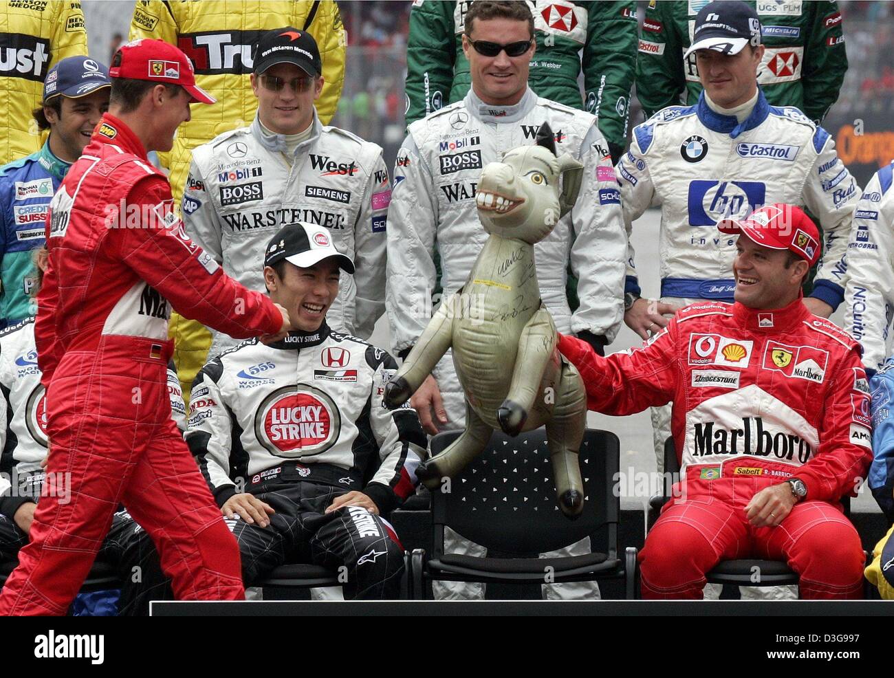 (dpa) -Ferrari's German Formula One world champion Michael Schumacher (L) arrives late as Formula One drivers pose for photographers prior to the start of the Brazilian Formula One Grand Prix at the Interlagos circuit in Sao Paulo, Brazil, Sunday 24 October 2004. Schumacher's Brazilian team mate Rubens Barrichello (R) holds an inflatable donkey from the 'Shrek' movie. Sitting in th Stock Photo
