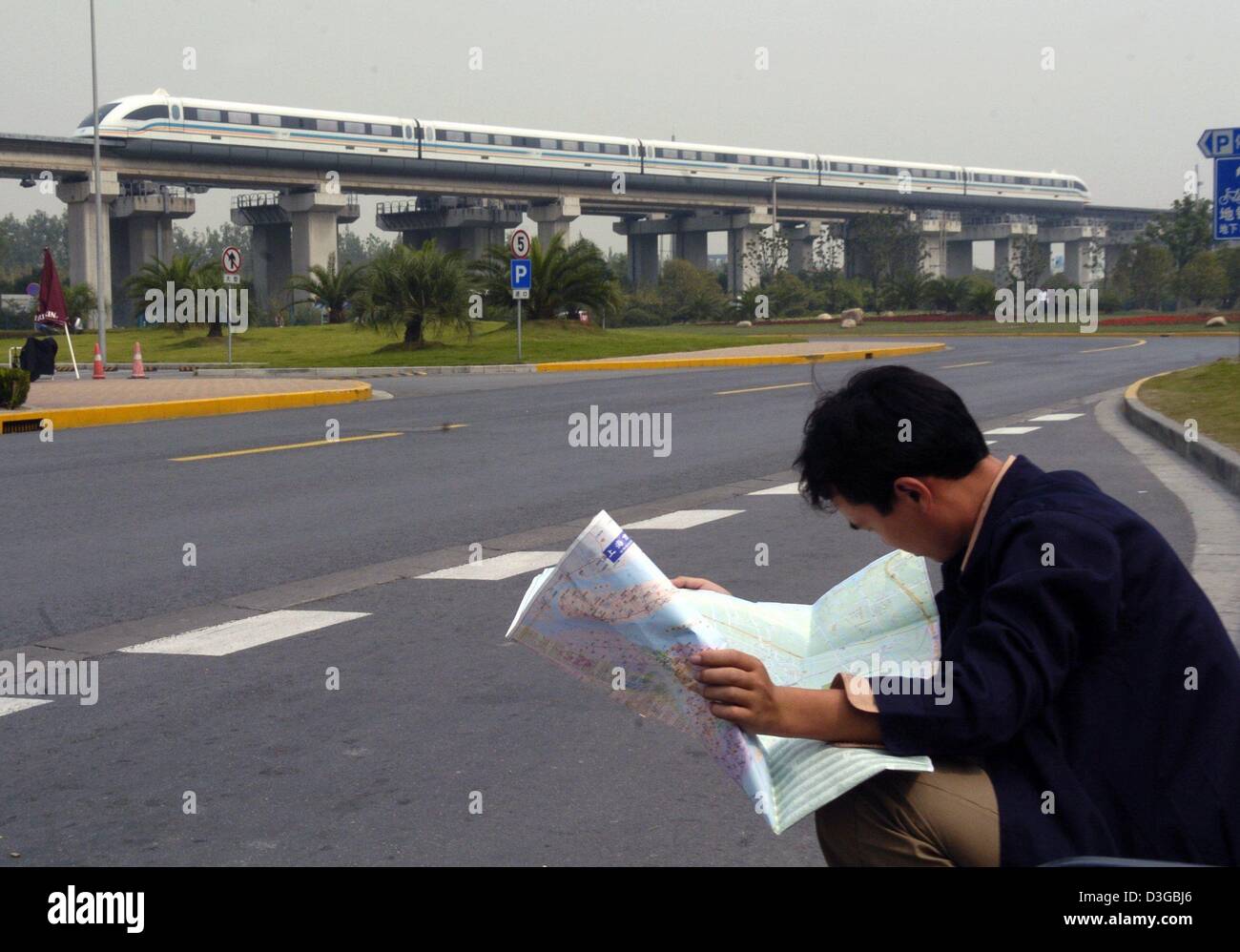 (dpa) - A Transrapid highspeed train races past a tourist who looks through a map in Shanghai, China, 11 October 2004. The up to 430 km/h fast train has been running in 20 minute intervals between the Shanghai fair grounds and the International Airport in Pudong since early 2004. The trip takes about 8 minutes. Stock Photo