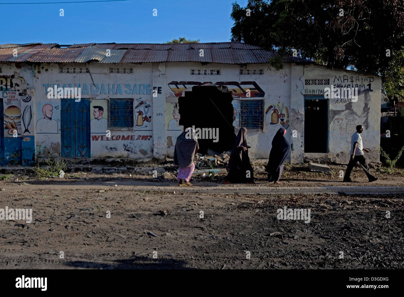 Three Somali women dressed in a hijab and a man walk past a disused war-torn building in downtown Mogadishu. Stock Photo