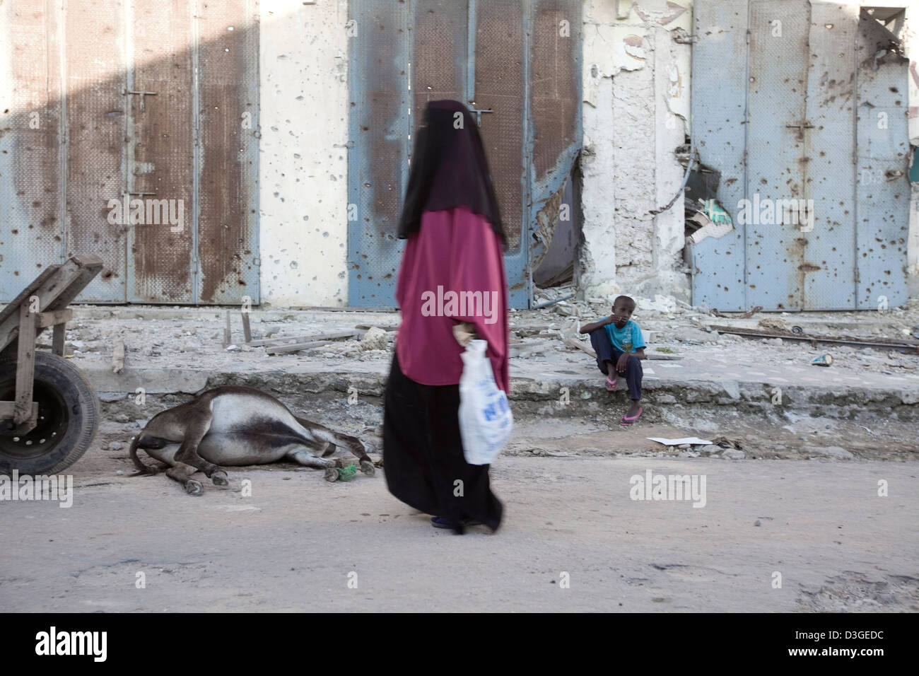 A hijab-clad woman walks past a dead donkey in downtown Mogadishu, Somalia. Stock Photo