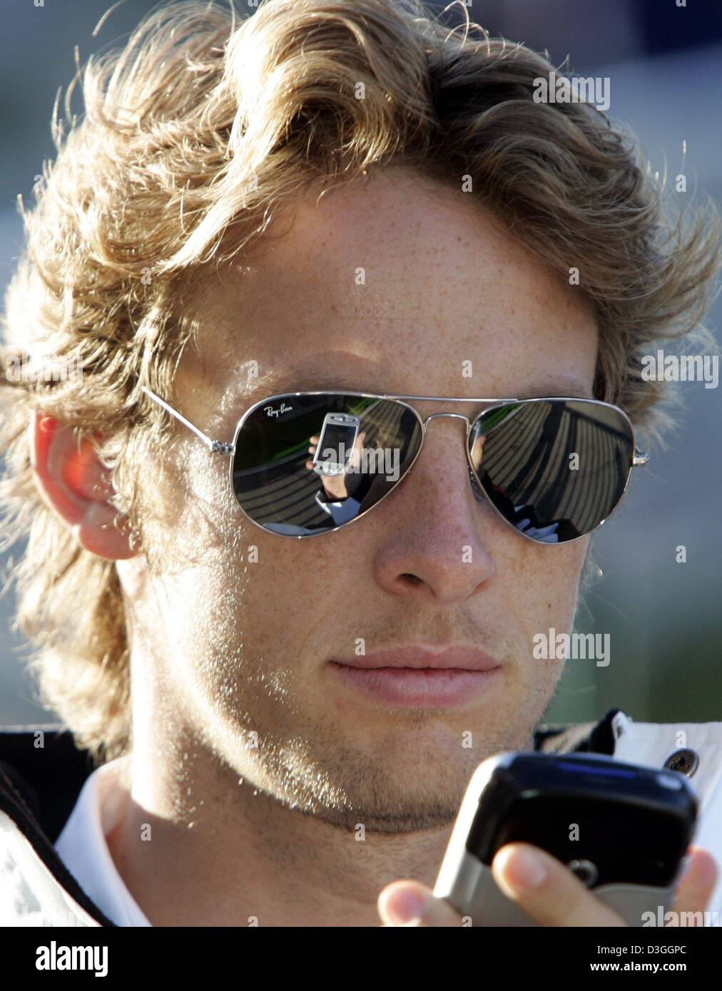 (dpa) - British formula one pilot Jenson Button (BAR Honda) looks on the display of his mobile phone on the formula one racing track in Spa-Francorchamps, Belgium, Friday, 27 August 2004. The Belgian Grand Prix will be held in Spa on Sunday, 29 August 2004. Stock Photo