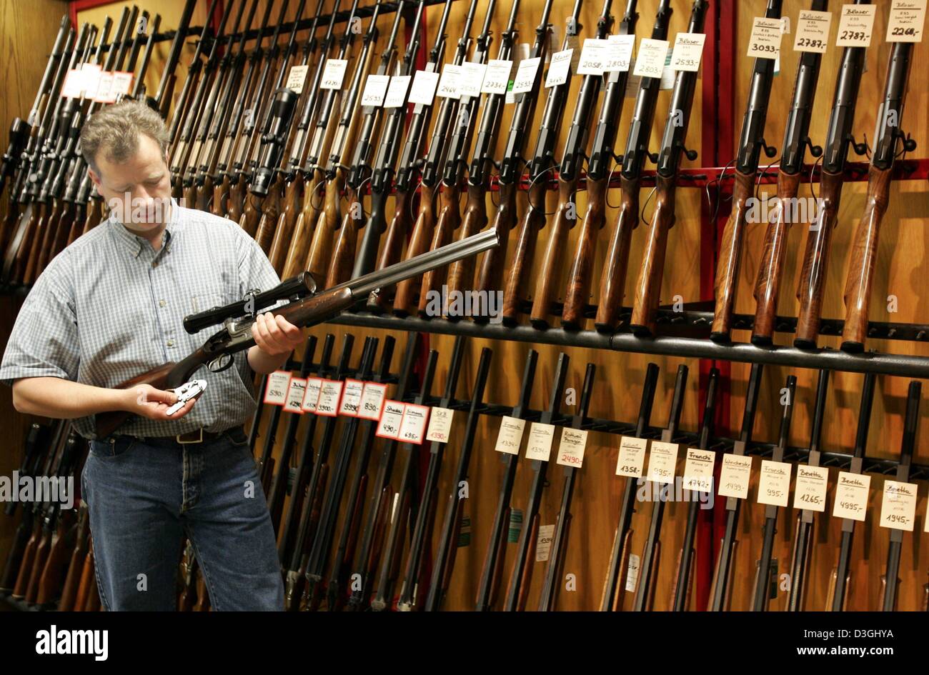 (dpa) - Stefan Knappworst, head of gunsmith Knappworst, inspects a rifle as he stands in front of wall with hunting rifles at the gunsmith's workshop in Braunschweig, Germany, 15 June 2004. There are around 30 traditional gunsmiths left in the state of Lower Saxony. The new gun law requires huntsmen and sports riflemen to keep their rifles locked up in special armour cabinets. Stock Photo