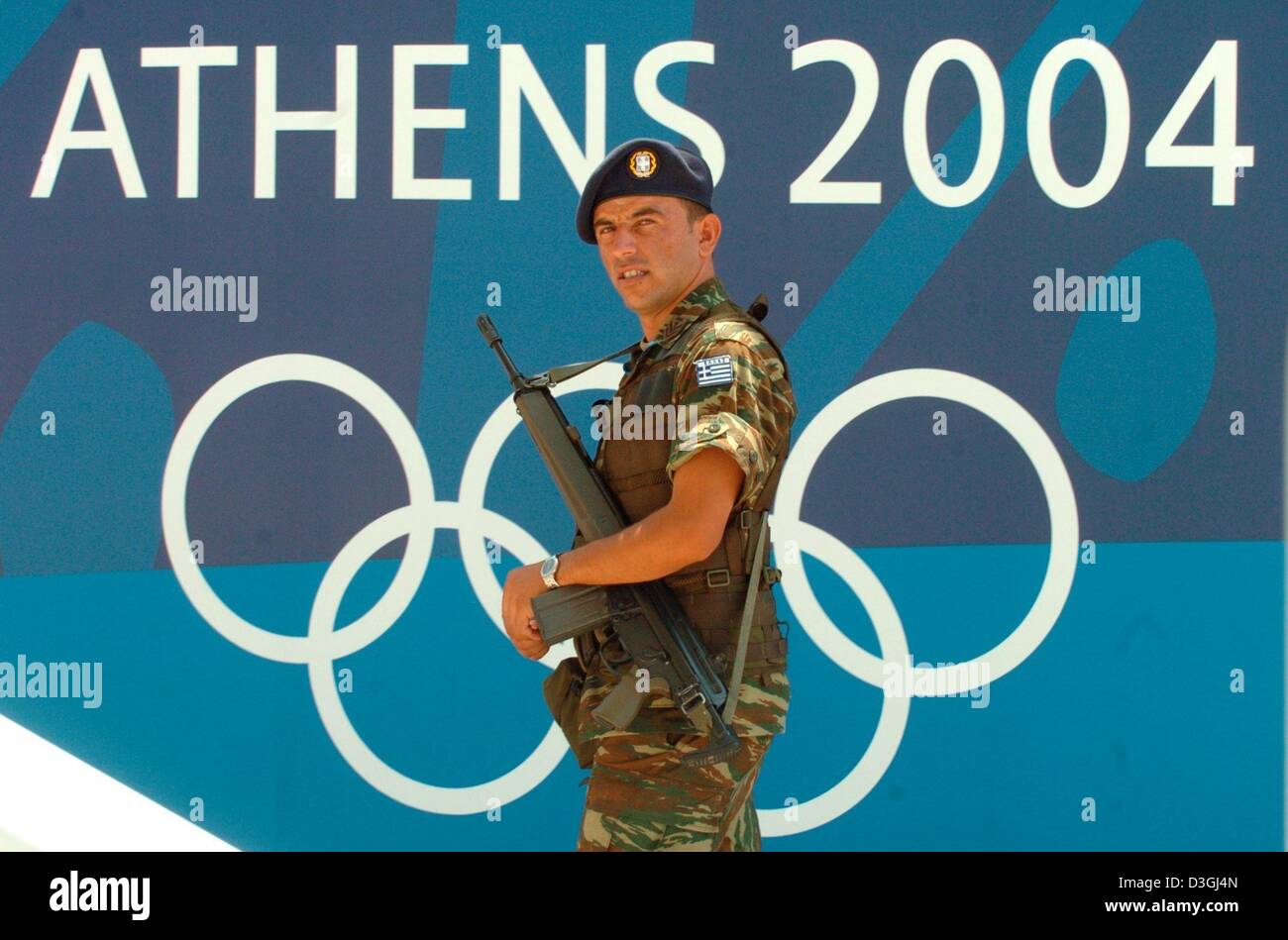 (dpa) - An armed soldier stands in front of the Olympic logo at the Olympic Rowing and Canoeing Centre in Schinias, Greece, 11 August 2004. With more than 10,800 athletes competing, the 2004 Summer Olympic Games will begin on Friday, 13 August 2004. Stock Photo
