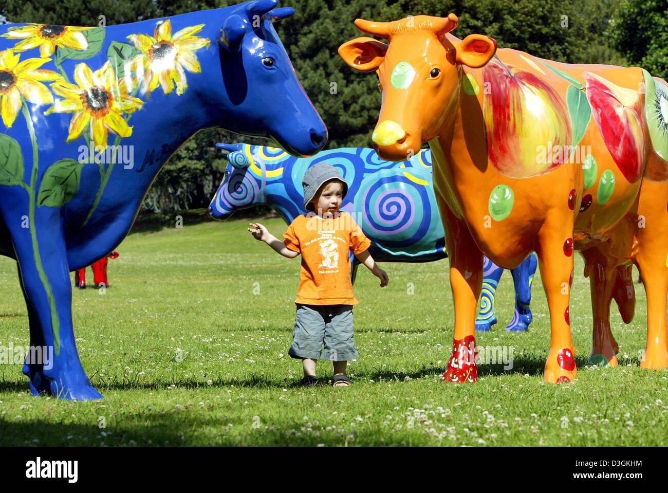 (dpa) - A small boy gazes at lifesized colourful cows made out of fibre glass at a park in Cologne, Germany, 17 July 2004. The 25 cows that were painted by four female artists are part of a travelling exhibition. The cows were manufactured at the workshop of Ulrike and Georg Kresken from Bocholt, Germany. Stock Photo