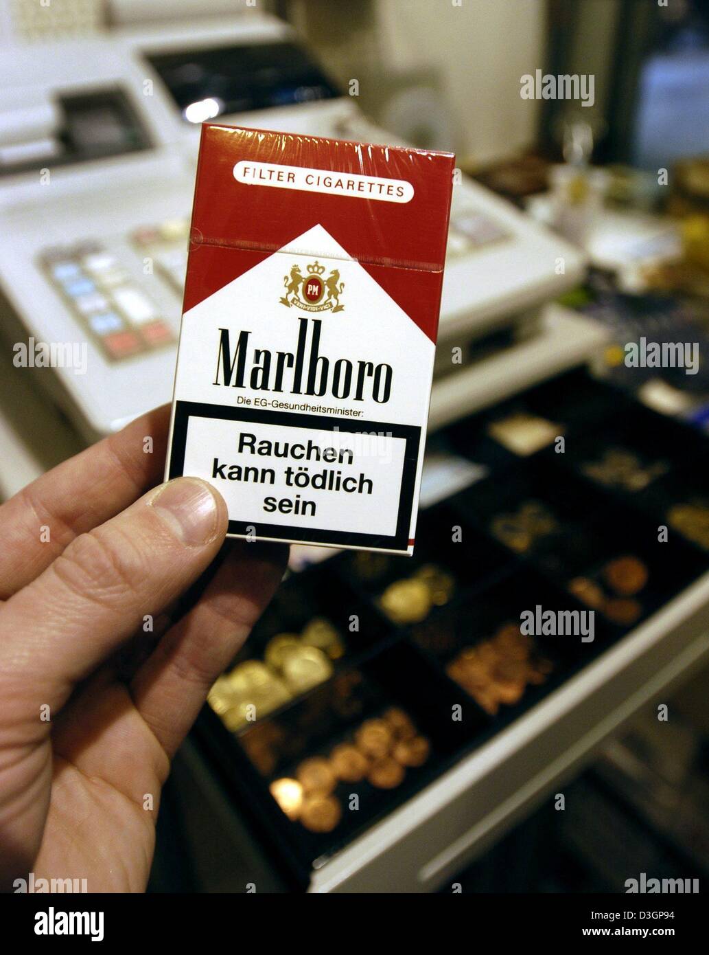 dpa) - A hand holds up a pack of Marlboro cigarettes in front of a cash  register in a tobacco shop in Regensburg, Germany, 4 March 2004. The  compulsory health warning on