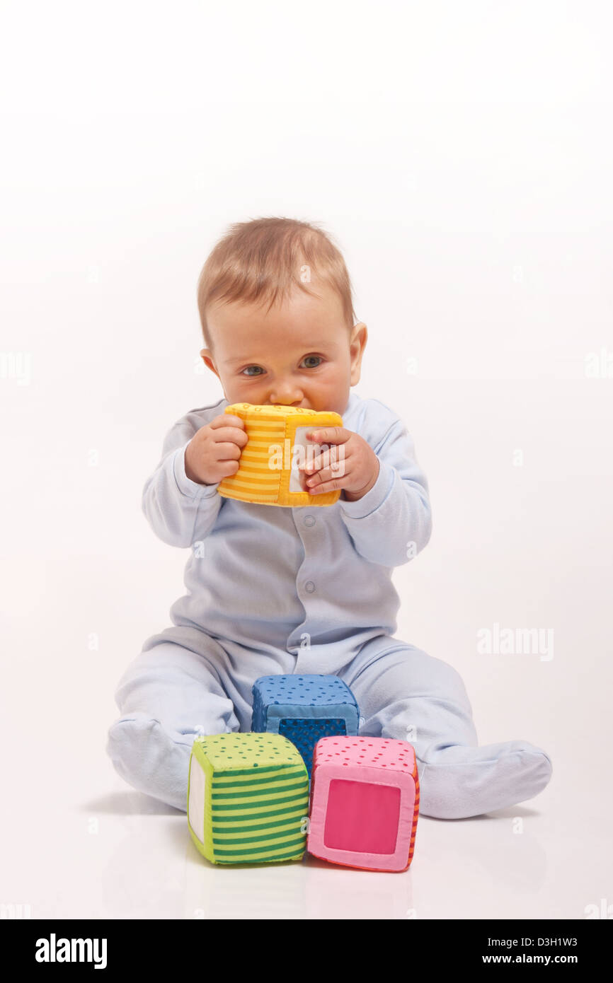 Baby boy in blue pajamas playing with color blocks on white background