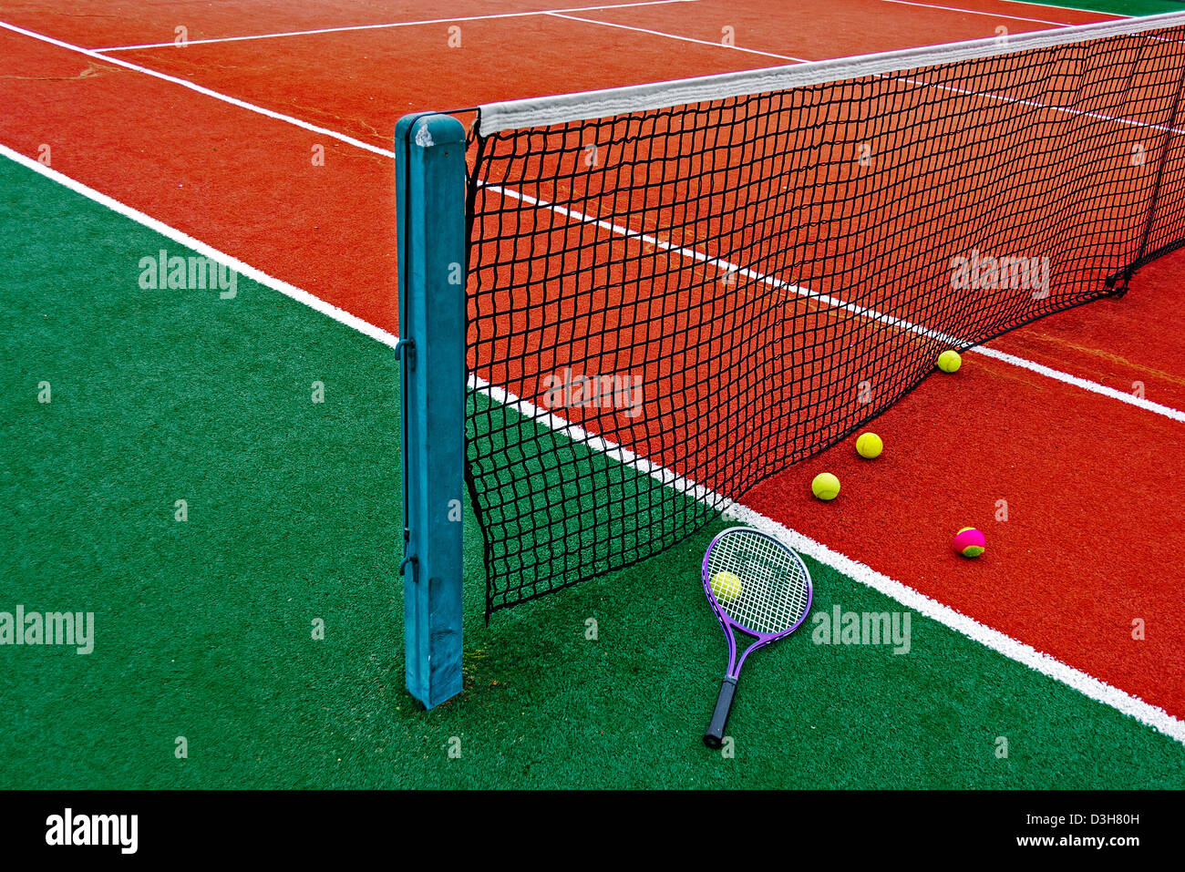 Ball and tennis racket arranged around the net on a synthetic field. Stock Photo