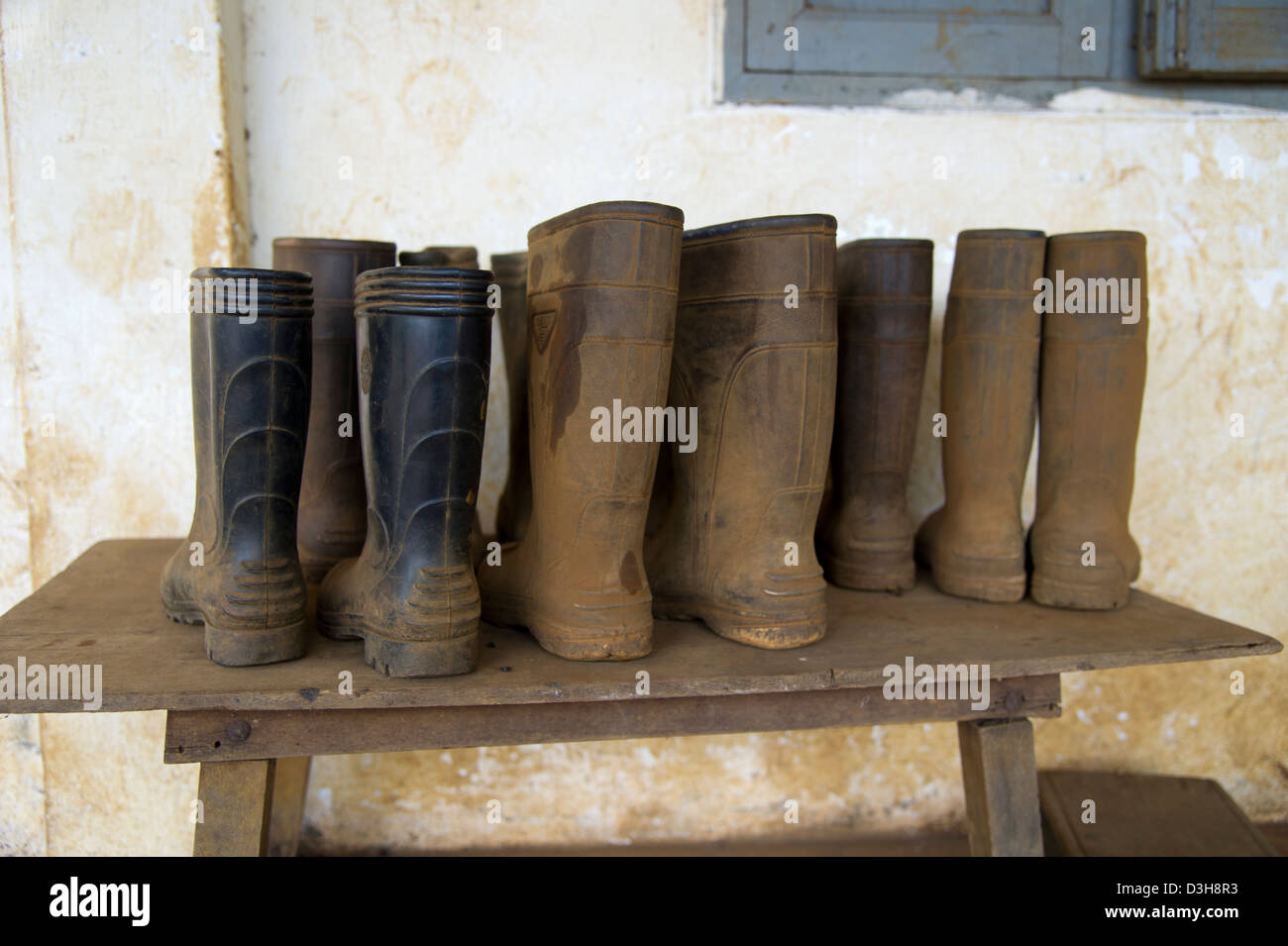Rubber boots covered in mud sit in rows on a wooden table Stock Photo