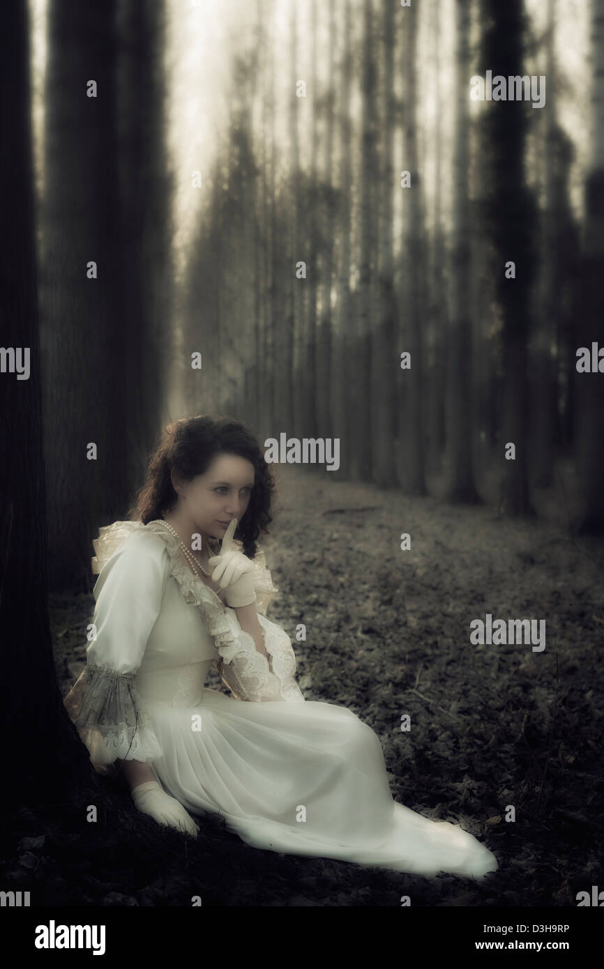 a woman in a victorian dress sitting in the woods, having a secret Stock Photo
