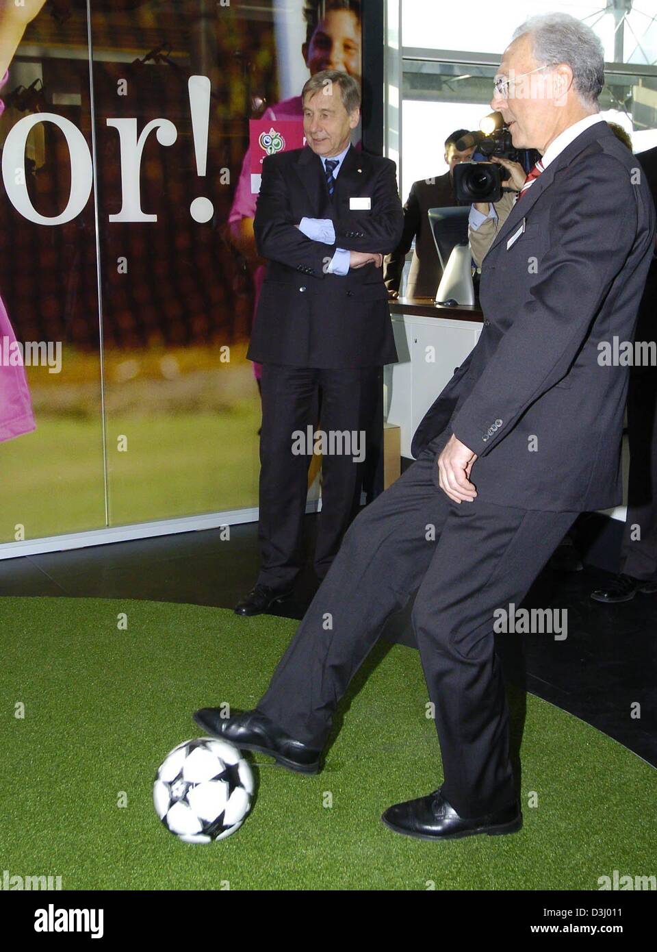 (dpa) - Franz Beckenbauer, president of the organising committee of the FIFA 2006 World Cup, kicks a ball while German Minister of Labour and Economy looks on at a stand of the Telekom AG during a World Cup 2006 investment conference in Leipzig, Germany, 22 January 2004. Participants of the conference discussed in workshops the various possibilities for business and investments in  Stock Photo