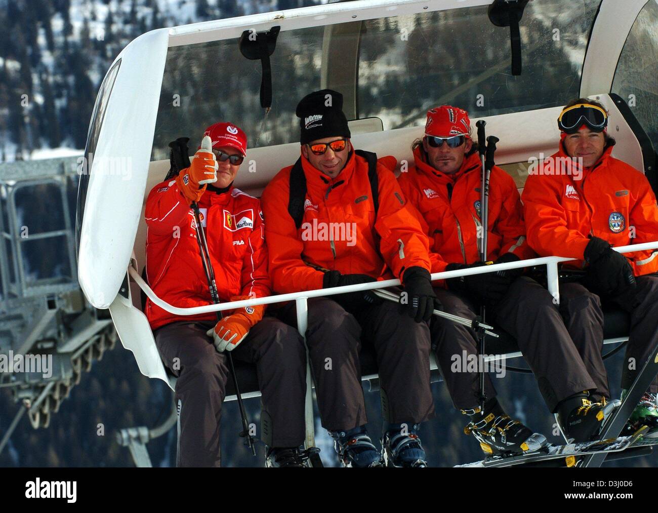 (dpa) - German formula one world champion Michael Schumacher (L) gives the thumbs up sign while being carried uphill in a chair-lift with his skiing instructor and bodyguards, near the ski resort Madonna di Campiglio, Italy, 15 January 2004. The Ferrari racing team in Madonna di Campiglio meets for a traditional skiing holiday under the motto 'Wrooom'. Stock Photo