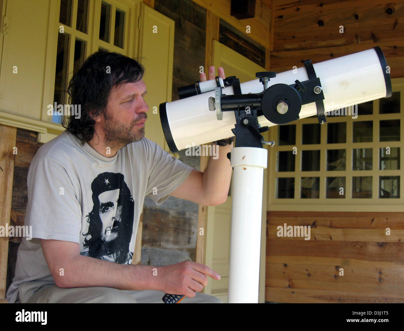 (dpa) - Bosnian film director Emir Kusturica looks through a telescope as he sits on the terrace of his house in the village of 'Kuestendorf', Serbia and Montenegro, 29 May 2005. Kusturica founded and built the village of 'Kuestendorf' as a centre for culture and science in the Serbian mountains. In its simplicity and humility the village is ment to represent an alternative counter Stock Photo