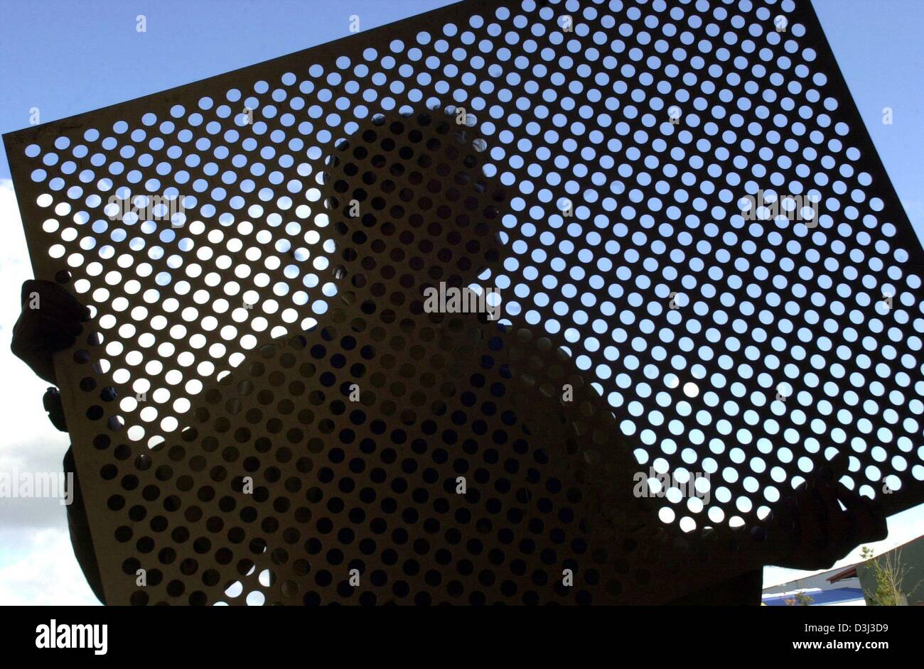 (dpa) - The silhouette of a worker who holds up a punched metal plate that will be used for a subway air-shaft at the Schmitz Lasertechnik company in Quitzow, Germany, 22 October 2003. The company specialises in cutting metal and steel parts with high-precision laser technology and punches. Stock Photo