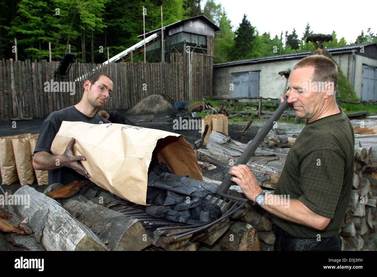 (dpa files) - Charburners Peter (R) and Sascha Feldmer fill the charcoal in paper bags on the compound of a charcoal plant in Hasselfelde, Germany, 16 May 2003. The charcoal plant is one of the last of its kind in Germany where charcoal is still produced in a traditional way. Stock Photo