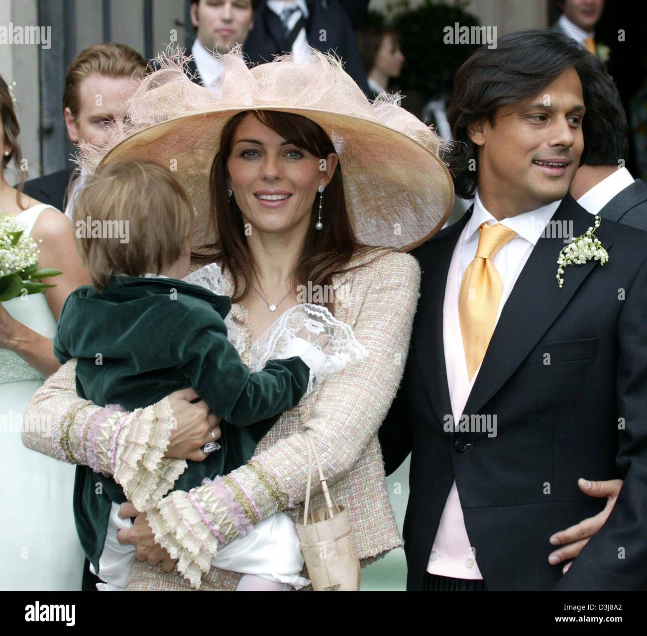 (dpa) - British actress and model Elizabeth Hurley (C) holds her son Damian in her arms as she arrives with her boyfriend Arun Nayer (R) to the wedding of Sven Ley and Zoe Appleyard at the cathedral in Salzburg, Austria, 8 May 2004. Stock Photo