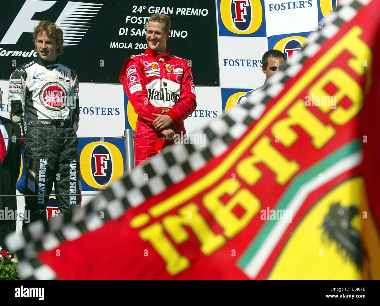 (dpa) - German formula one pilot and world champion Michael Schumacher (Ferrari) smiles as he stands between British formula one pilot Jenson Button (L) (BAR Honda) and Colombian pilot Juan Pablo Montoya (R) (BMW Williams), covered by a Ferrari flag, on the podium after the San Marino grand prix in Imola, Italy, 25 April 2004. Schumacher won the race ahead of Button and Colombian f Stock Photo