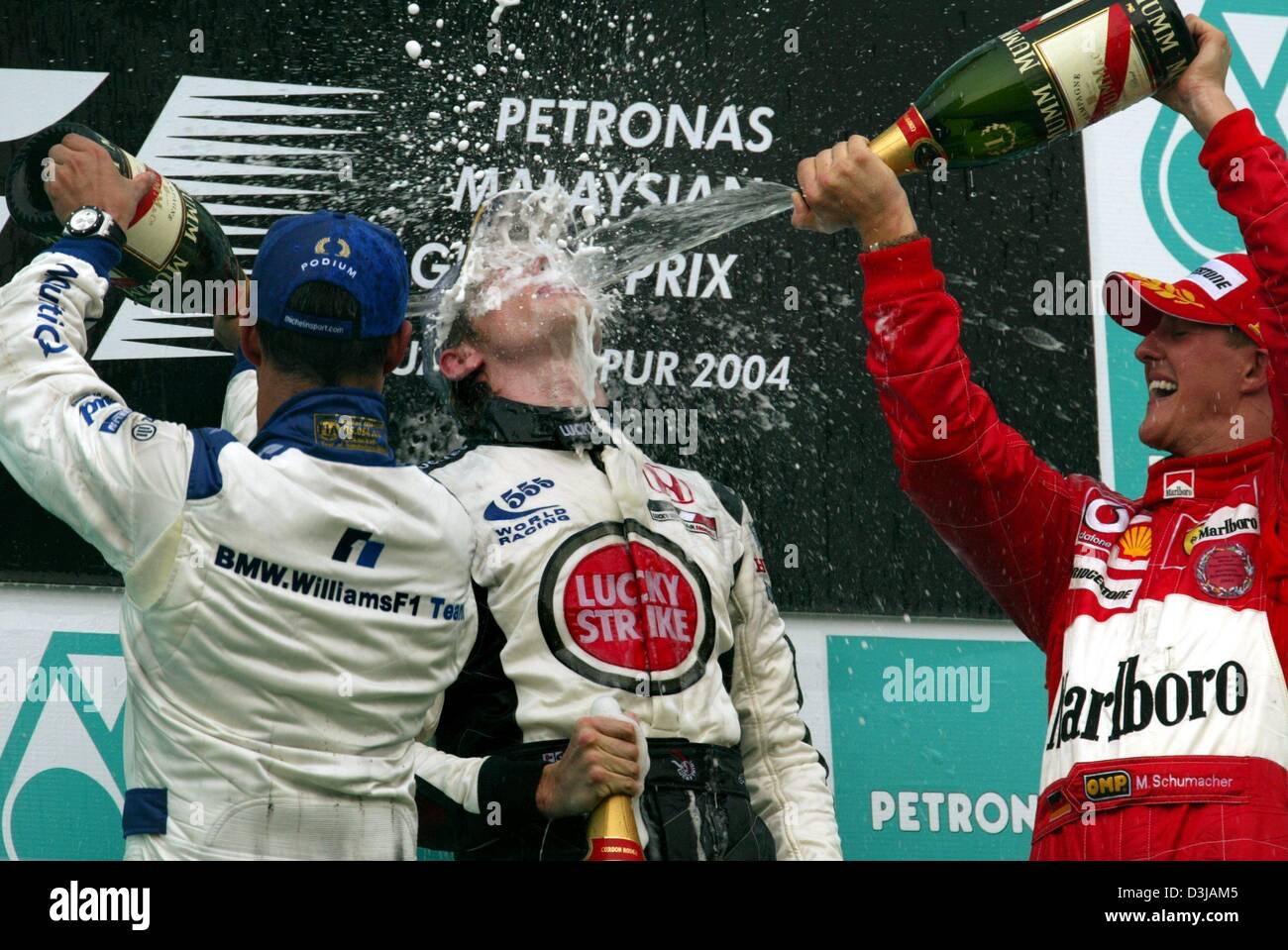(dpa) The German F1 world champion Michael Schumacher (Ferrari) sprays third placed Jenson Button (BAR-Honda/middle) with champagne after winning the Grand Prix of Malaysia on the Sepang racetrack near Kuala Lumpur on Sunday, 21 March 2004. Second placed Colombian F1 pilot Juan Pablo Montoya (BMW-Williams/left) joins the action. Schumacher gained his second victory in the second ra Stock Photo