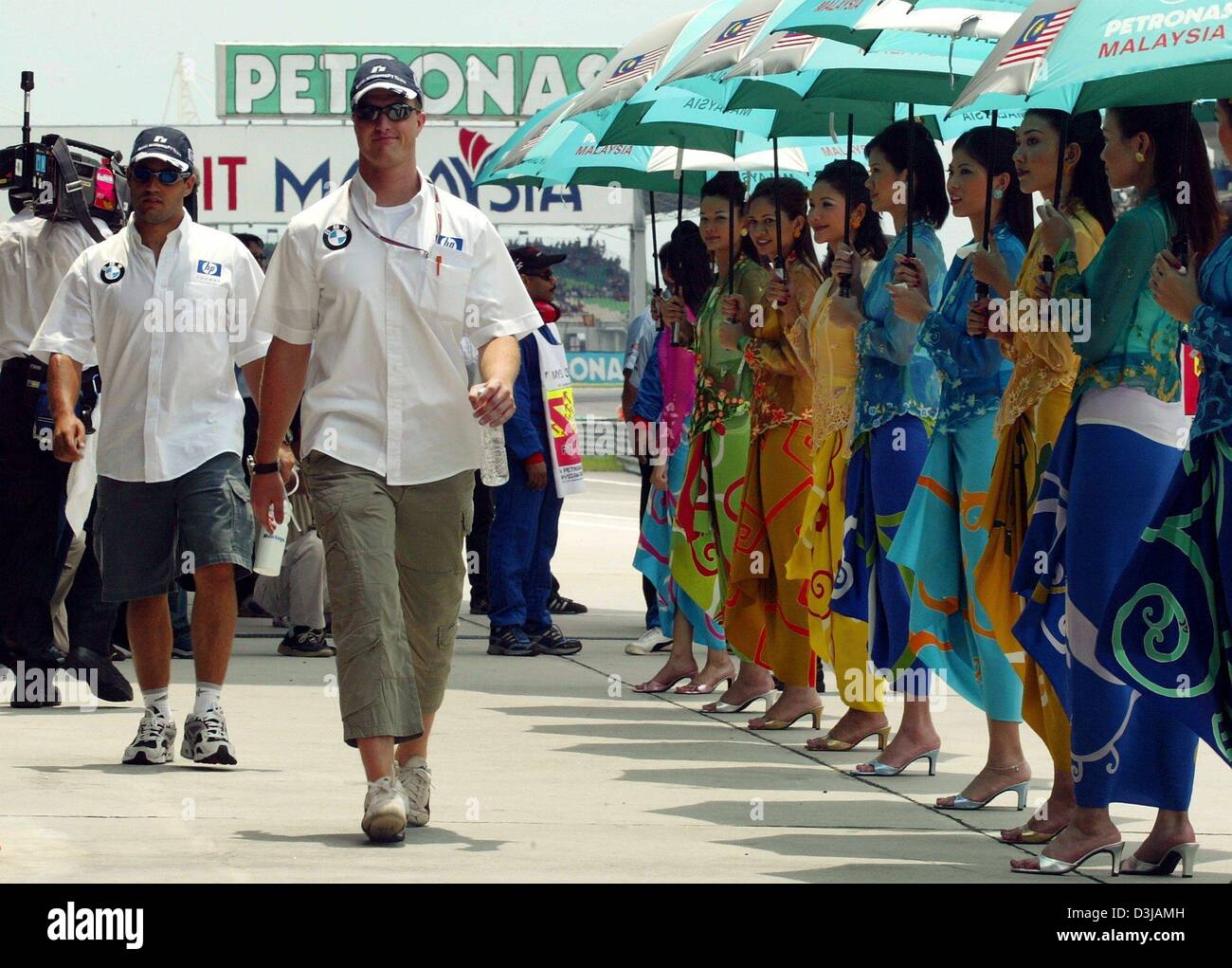 (dpa) Malaysian grid girls with umbrellas and traditional Malay clothes are lined up as German F1 pilot Ralf Schumacher (middle/ BMW-Williams) and Colombian F1 pilot Juan Pablo Montoya (left/ BMW-Williams) walk past them before the start of the Grand Prix of Malaysia at the Sepang racetrack near Kuala Lumpur on Sunday, 21 March 2004. Stock Photo