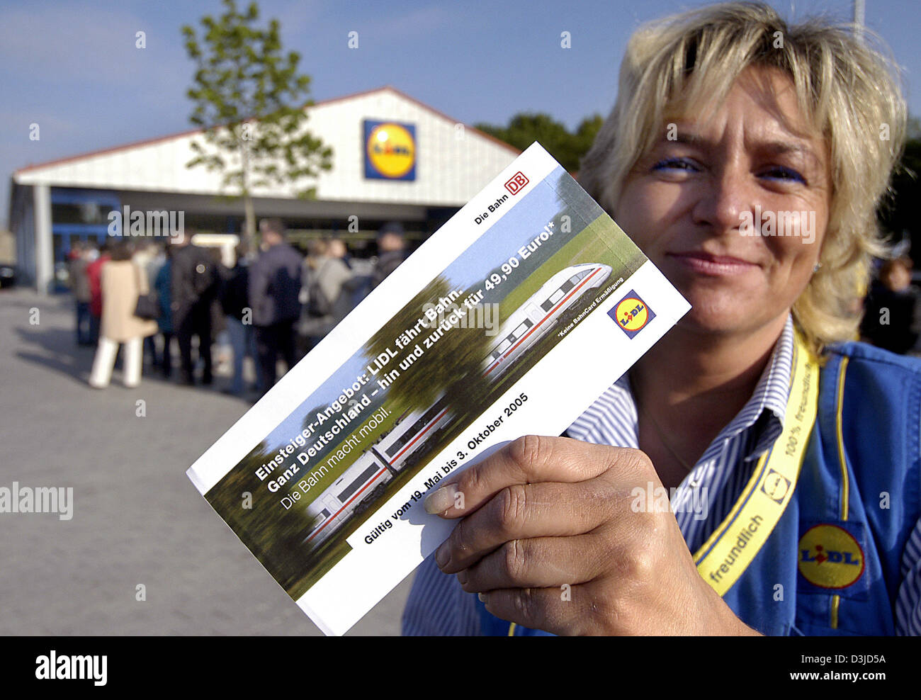 (dpa) - Sales assistant Ramona Wienholz presents a train ticket as she stand in front of a branch of German discount retailer Lidl in Augsburg, Germany, Thursday, 19 May 2005. A group of customer queue outside the entrance.  Lidl stores are now selling train tickets for the first time. In some of the company's branches the tickets went out of stock within minutes. Stock Photo