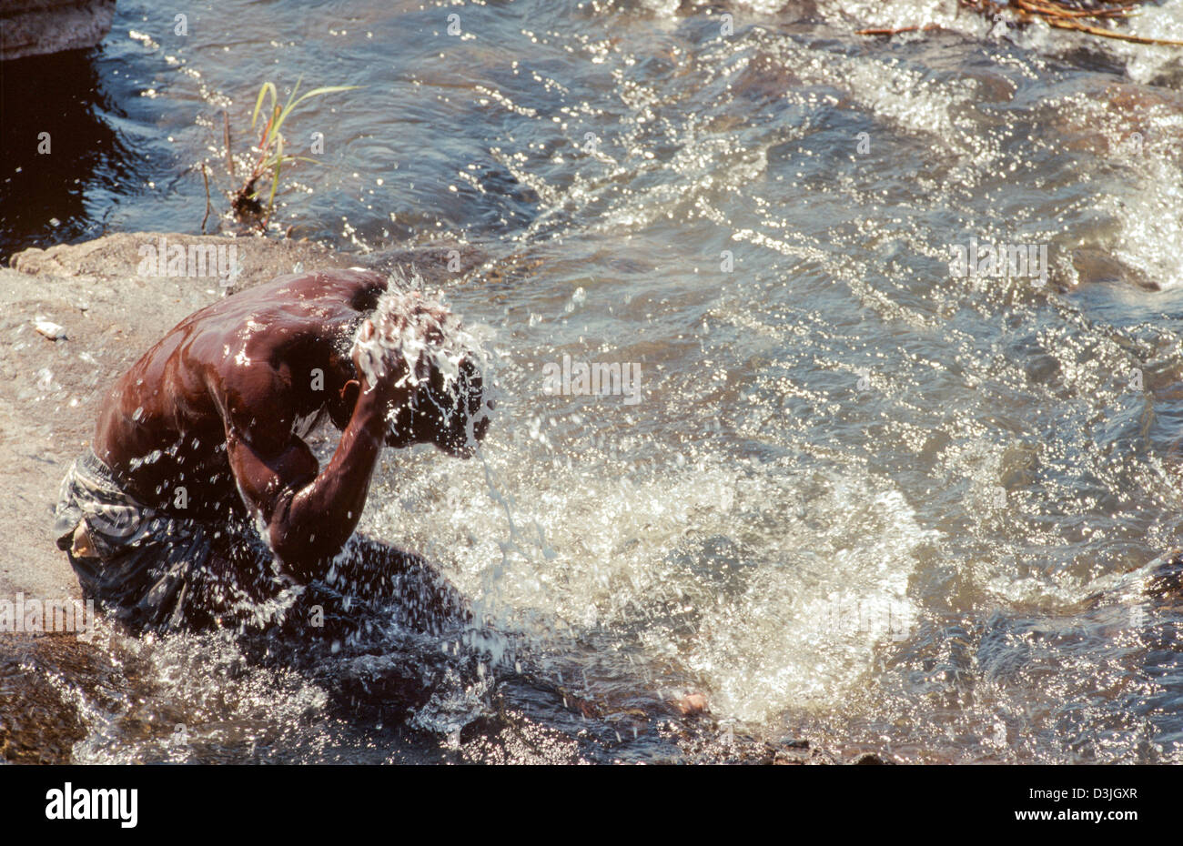 Man sitting on a riverside rock, washing himself in the River Limpopo ...