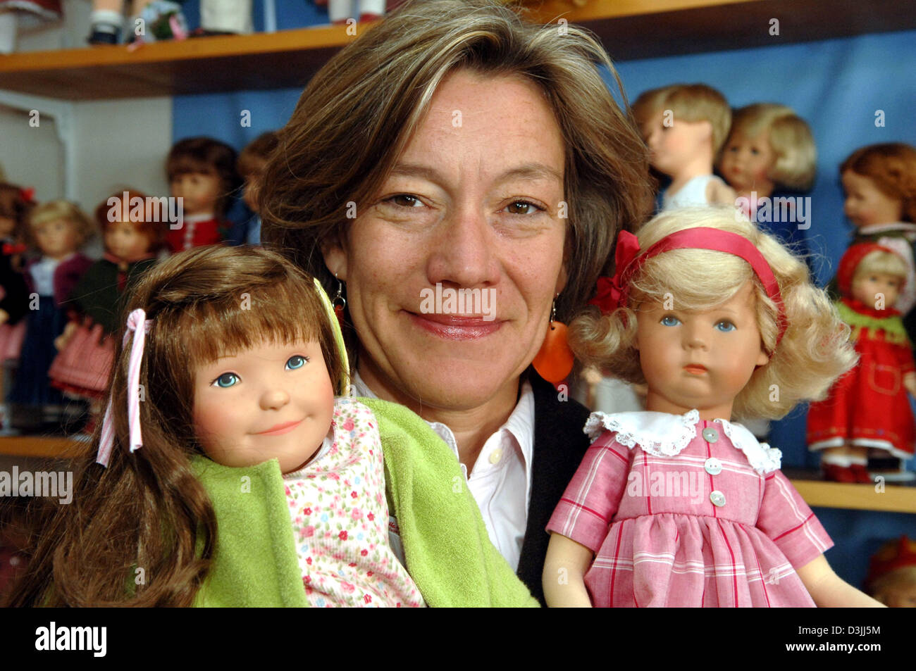dpa) - Business manager of 'Kaethe-Kruse-Dolls' Andrea Kathrin Christenson  poses with two dolls in front of the picture of Kaethe Kruse (1883-1968),  foundress of the company, in Donauwoerth, Germany, 11 April 2005.