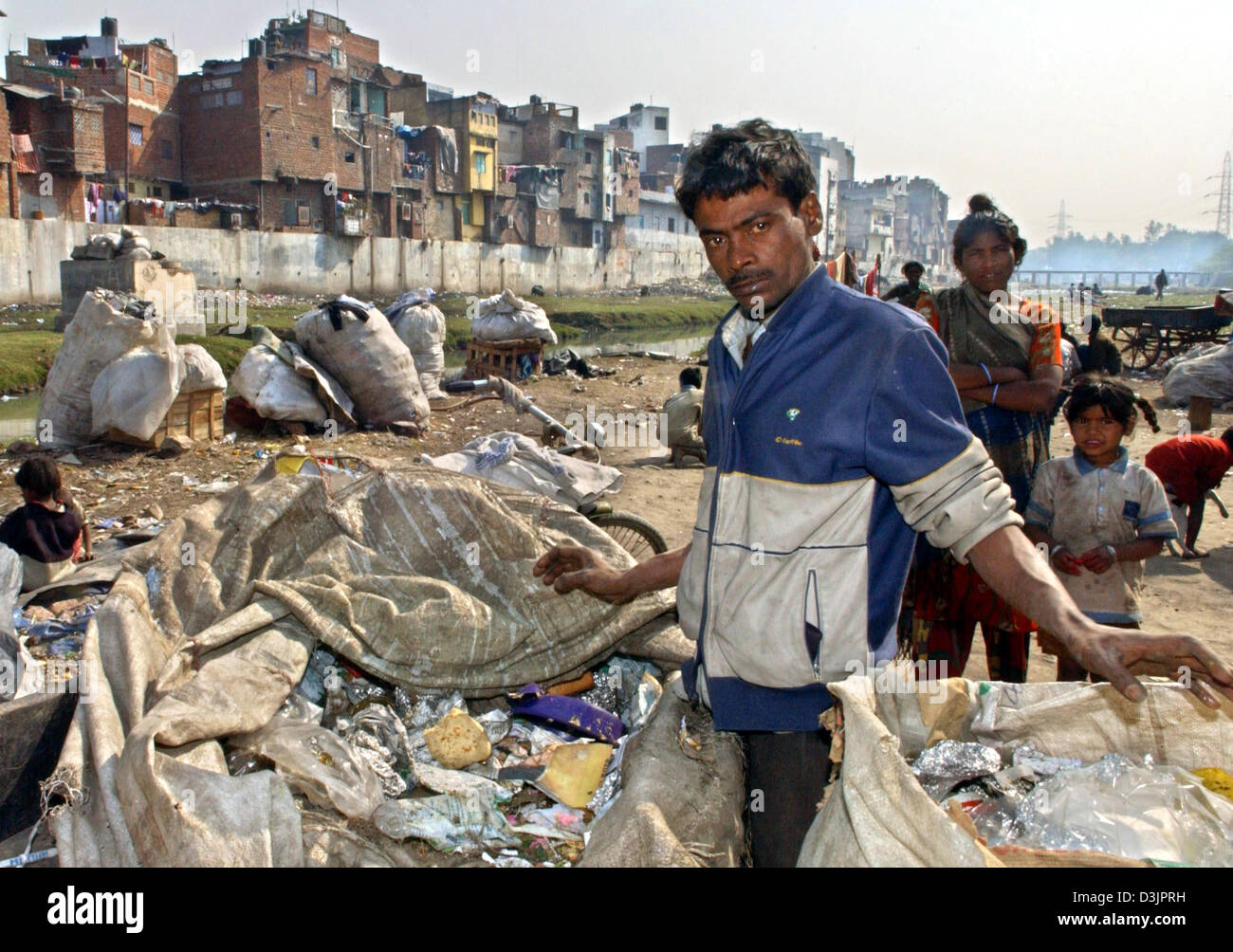 (dpa) - A man stands between bags of waste and rubbish in a slum on the outskirts of metropolitan Delhi, India, 02 February 2005. While modern high-rises are being built in the business districts of India's inner cities, countless Indians still live in poverty in a country with more than one billion people. Stock Photo