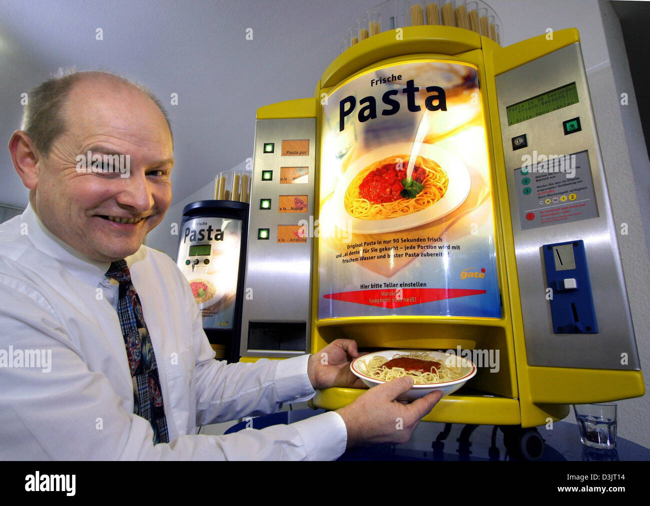 (dpa) - Inventor and chartered engineer Thomas Boden collects a dish of freshly cooked spaghetti and tomato sauce from his vending machine 'Cucina 2000+' (back) at his company in Woellstadt, Germany, 17 January 2005. The machine cooks pasta in record time of only 90 seconds by using a patented procedure, always using fresh water for cooking and in addition also delivers three ready Stock Photo