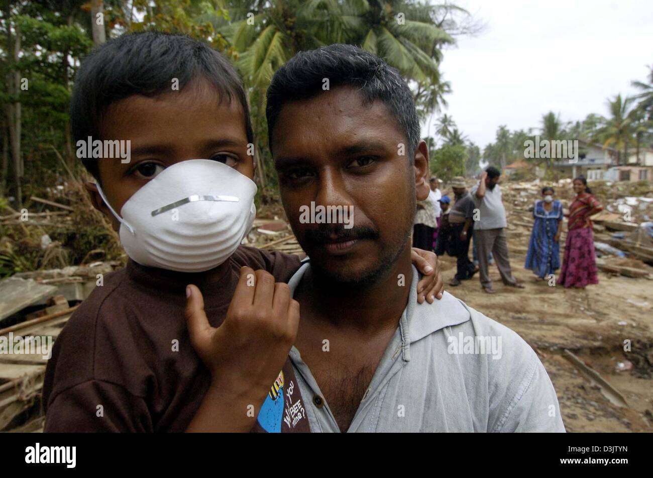 (dpa) - A father carries his son who is wearing a mask in fear of epidemics in the town of Dellewatha near the city of Galle, Sri Lanka, 2 January 2005. Hundreds of thousands of people living in the coastal areas of Sri Lanka lost their homes and around 30,000 people were killed by a devastating tsunami caused by a seaquake on 26 December 2004. Stock Photo