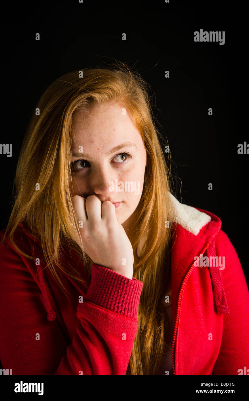 A shy nervous 16, 17 year old red haired freckle faced teenage girl, biting her finger nails UK Stock Photo