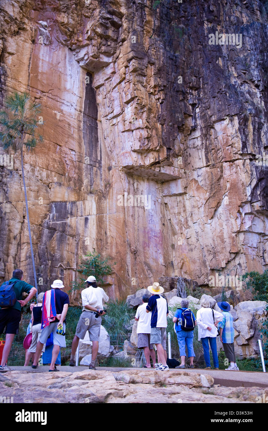 Tourists pause for a look at a panel of ancient Aboriginal rock art on a sandstone cliff face, Nitmiluk NP, Australia Stock Photo