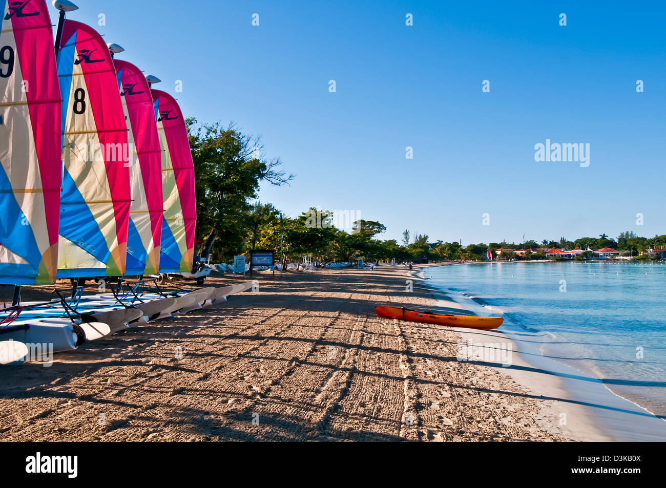 Line of catamaran sailboats with colorful sails early morning on Negril beach and kayak at the water Stock Photo
