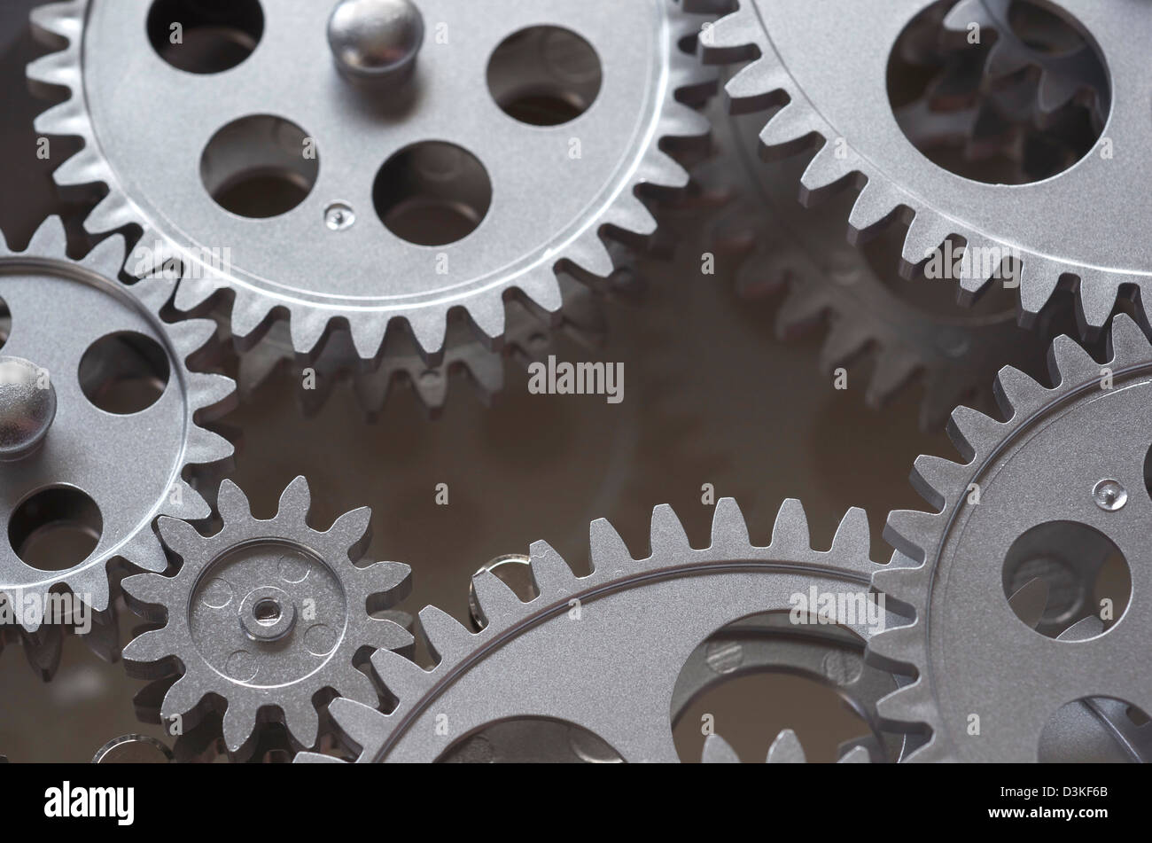 Gears interlocked that are gray, and around the perimeter of the frame with darker reflective area in the center. Stock Photo