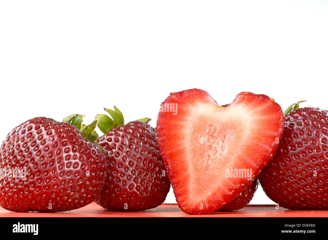 Four strawberries, one of them cut in half and having a heart-shape look. Stock Photo