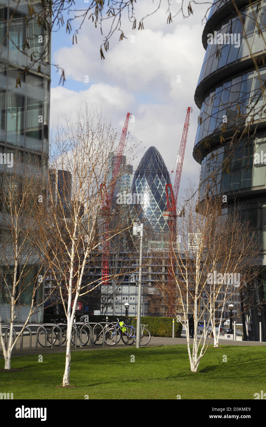 The Gherkin city buildings and construction cranes glimpsed through City Hall and office buildings South Bank, London, UK, GB Stock Photo