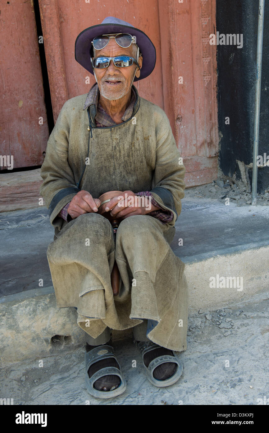 Elderly pilgrim wearing two pairs of sunglasses, sitting outside of Lamayuru Gompa, (Ladakh) Jammu & Kashmir, India Stock Photo