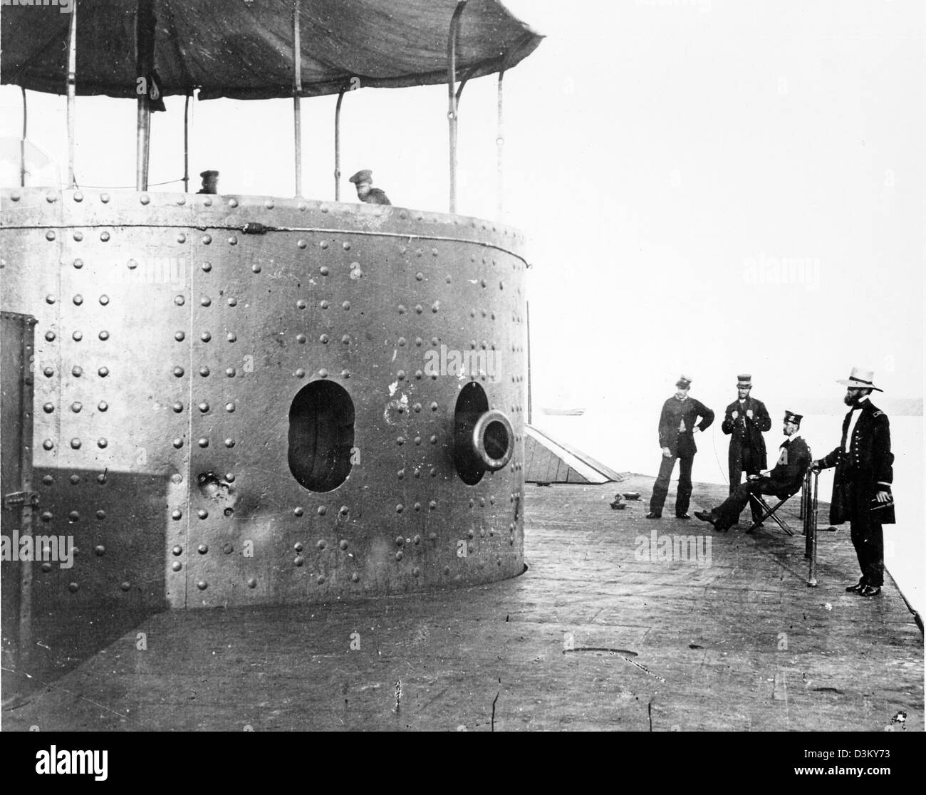 Undated photograph showing the USS Monitor deck looking forward on the starboard side, while the ship was in the James River in Virginia, July 9, 1862. The turret, with the muzzle of one of Monitor's two 11-inch Dahlgren smoothbore guns showing, is at left. Note dents in turret armor from hits by Confederate heavy guns and crewmembers atop the turret. Officers (left to right): Third Assistant Engineer Robinson W. Hands, Acting Master Louis N. Stodder, Second Assistant Engineer Albert B. Campbell (seated) and Acting Volunteer Lieutenant William Flye (with binoculars). Stock Photo
