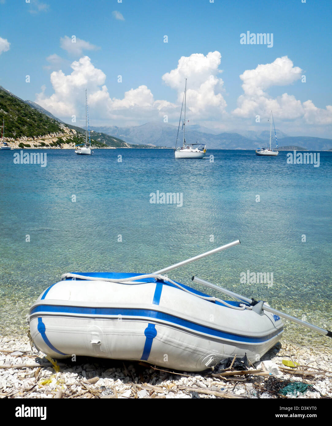 A dinghy pulled up on a stony beach, from a yacht in the background, in