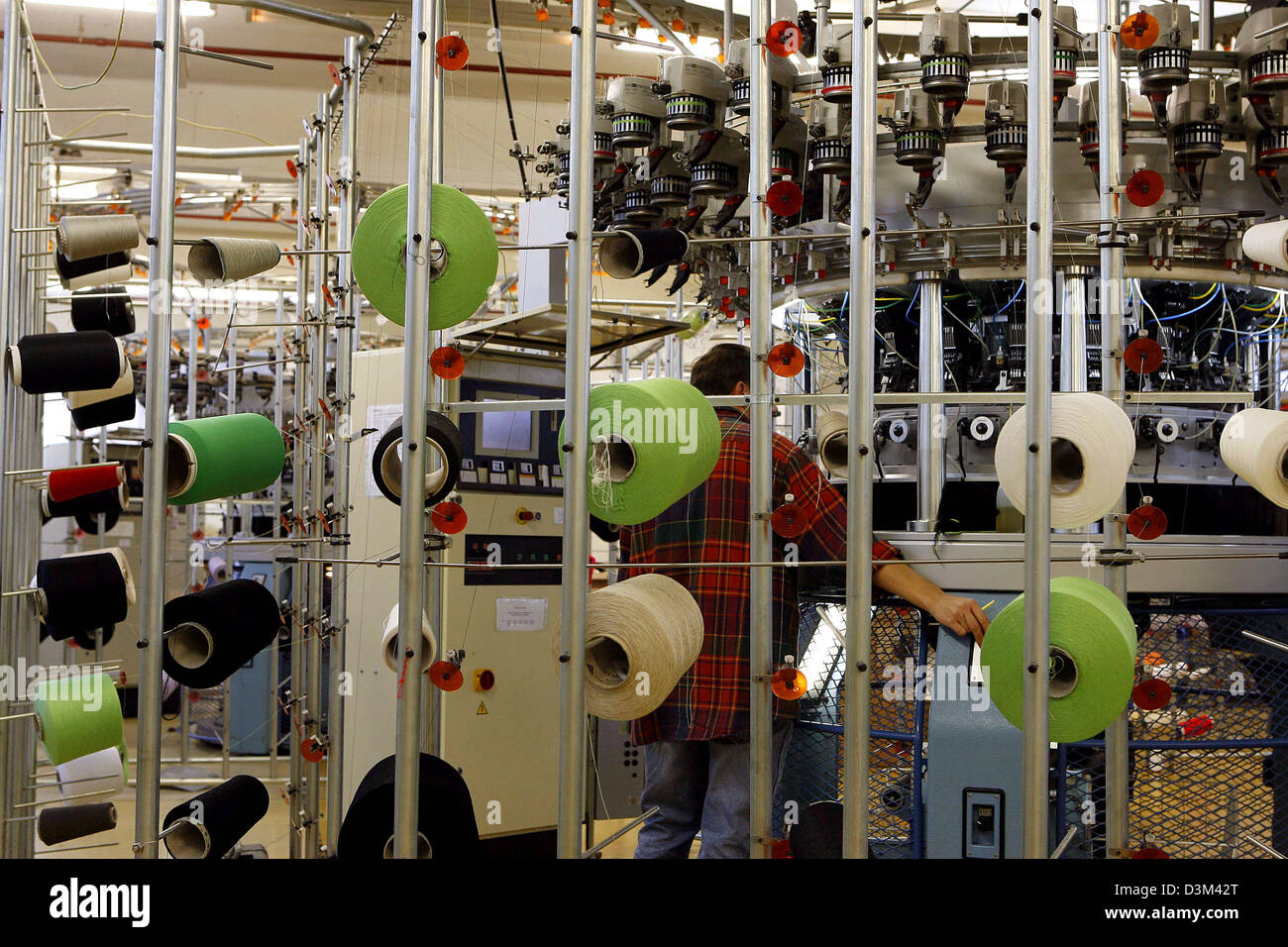 (dpa) A technician inspects a knitting machine as he stands behind a