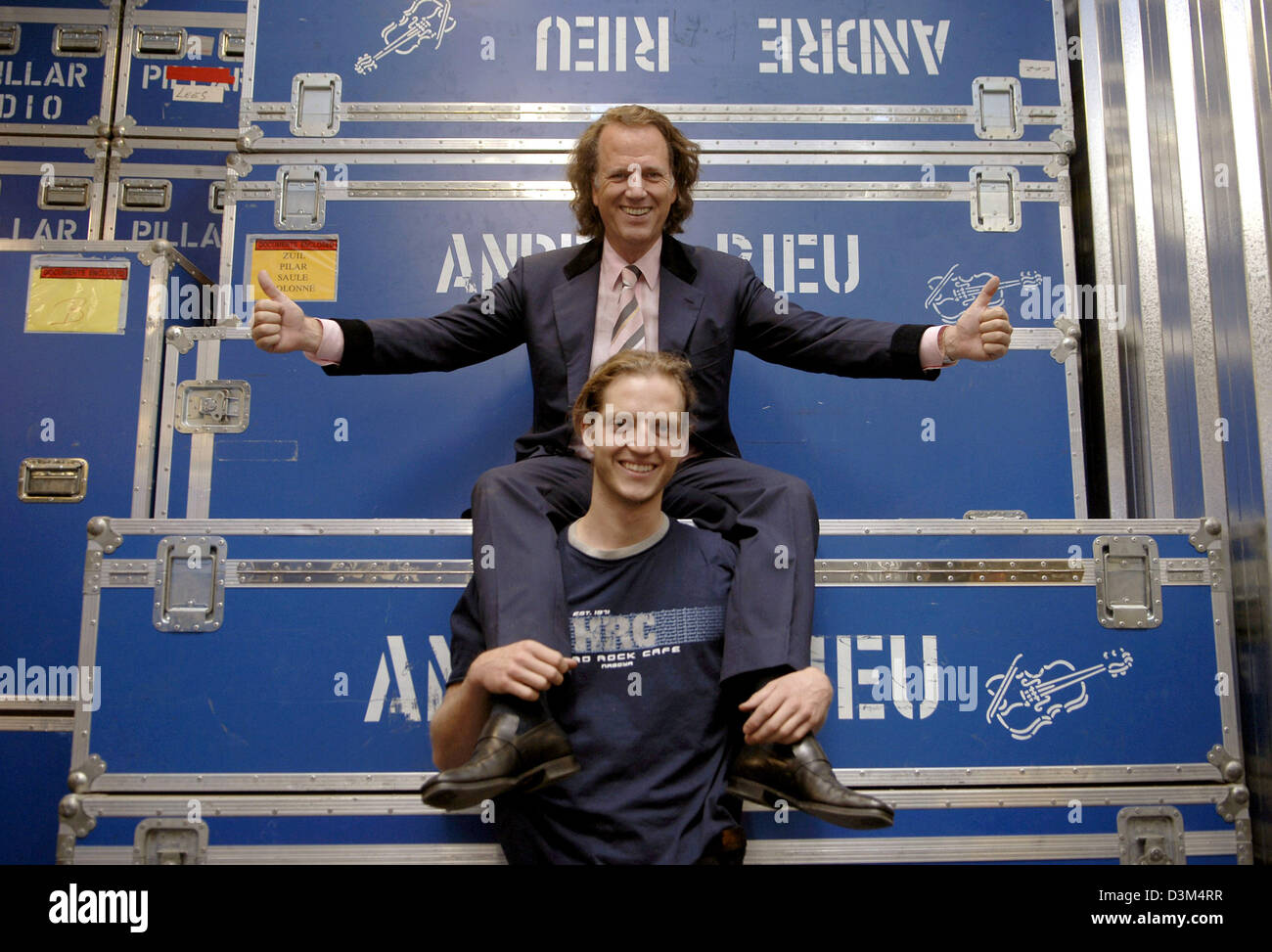 (dpa) - Dutch star violinist Andre Rieu (top) and his son Pierre (24) pose in front of large containers featuring Andre Rieu's name at his warehouse in Maastricht, the Netherlands, 02 November 2005. The 56-year-old musician is about to start the first part of his tour through Canada and the USA, where he will perform at 13 mayor cities. The complete equipment of his crew, which num Stock Photo