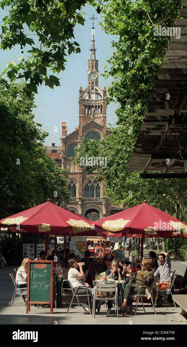 (dpa files) - Tourists enjoy drinks in a sidewalk cafe in front of the main building of the  'Hospital de Santa Creu i Sant Pau', featuring a spire with a clock and a colourful mixture of mediaeval and arabic ornaments shaping the art nouveau architectural style of the building in Barcelona, Spain, 11 June 2002. Initially financed from the inheritance money of Catalan banker Pau Gi Stock Photo