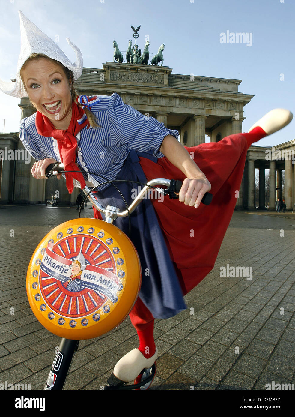 (dpa) - A model dressed as the advertising persona Frau Antje 'Miss Antje' poses with a bicycle and a loaf of cheese in front of the Brandenburg Gate in Berlin, Thursday, 12 January 2006. The 71st International Green Week agricultural fair runs from 13 January to 22 January 2006. Photo: Wolfgang Kumm Stock Photo