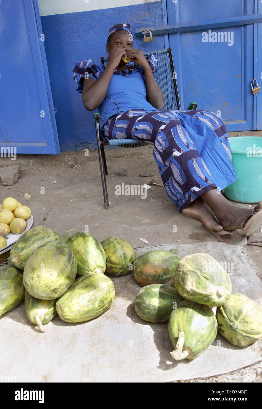 A fruit vendor in a blue dress sits beside a heap of melons in the ...