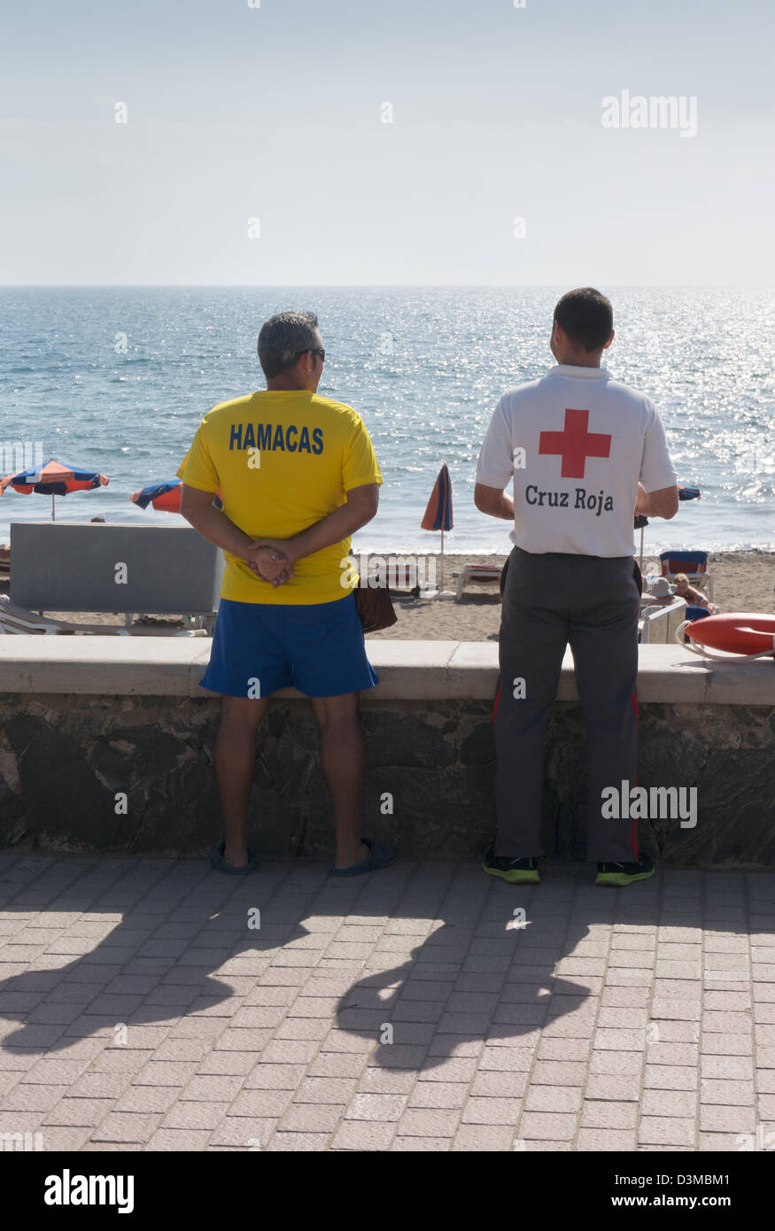 Two men, one Cruz Roja life guard, looking out to sea Meloneras, Maspalomas, Gran Canaria Stock Photo