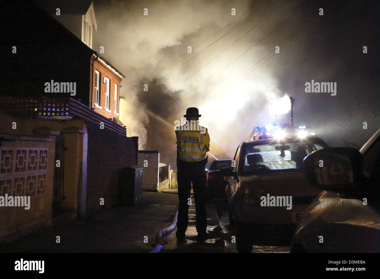 A police woman watches as firemen extinguish a fire in a house in