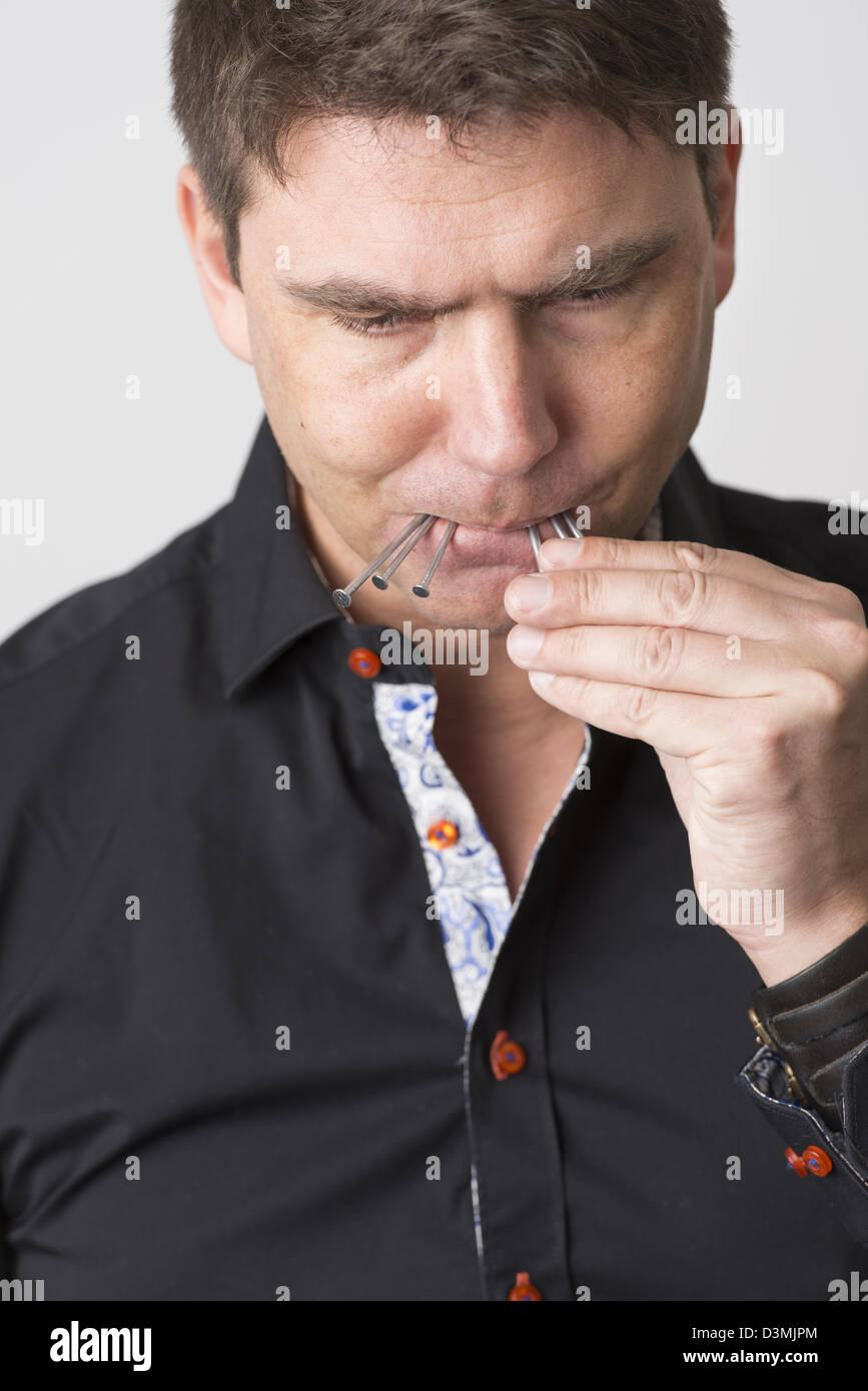 Pensive adult male holds metallic nails in his mouth. Stock Photo