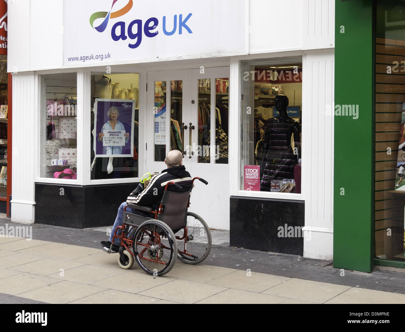 Old age an elderly man waits patiently outside an Age UK Charity shop