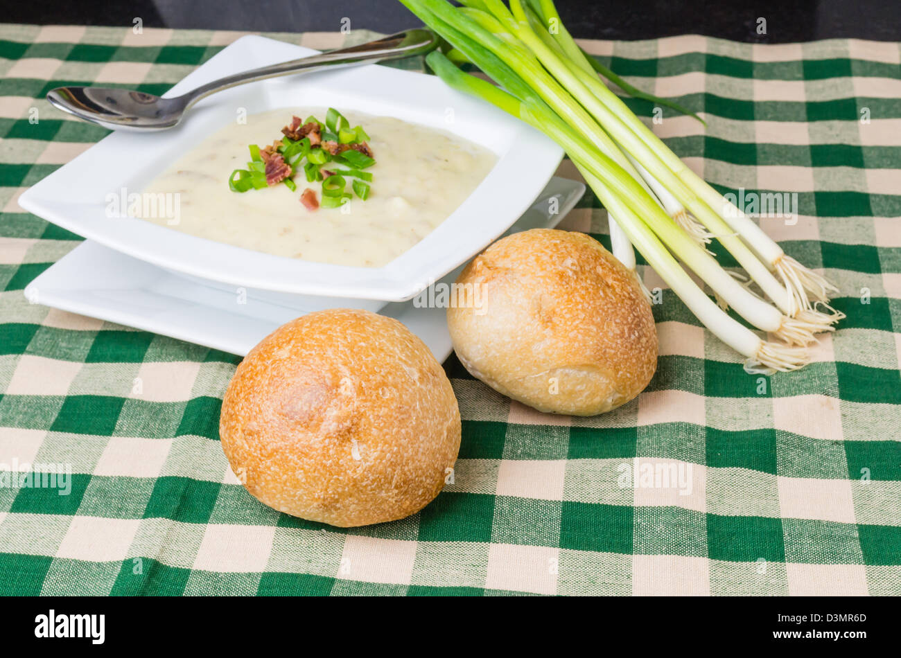 A bowl of hearty potato leek soup with green onions for garnish and wheat rolls Stock Photo
